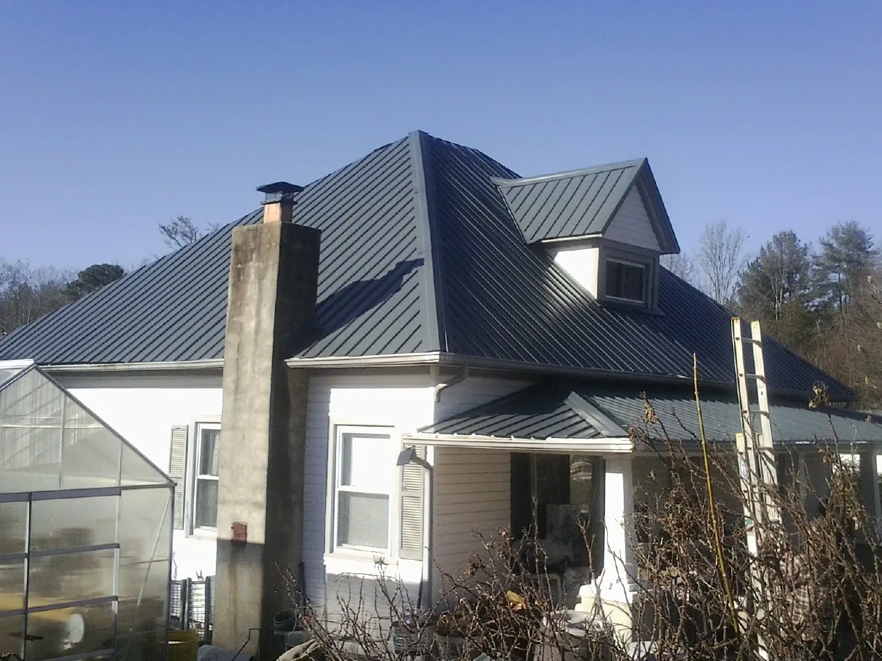 Dark blue standing seam metal roof on a white farmhouse with dormer in South Plymouth