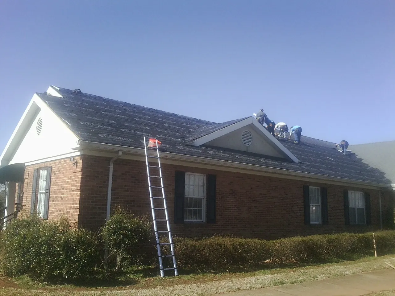Crew tearing shingles off a brick ranch roof with a ladder set — Metal Roof Repair work by our crew in South Plymouth