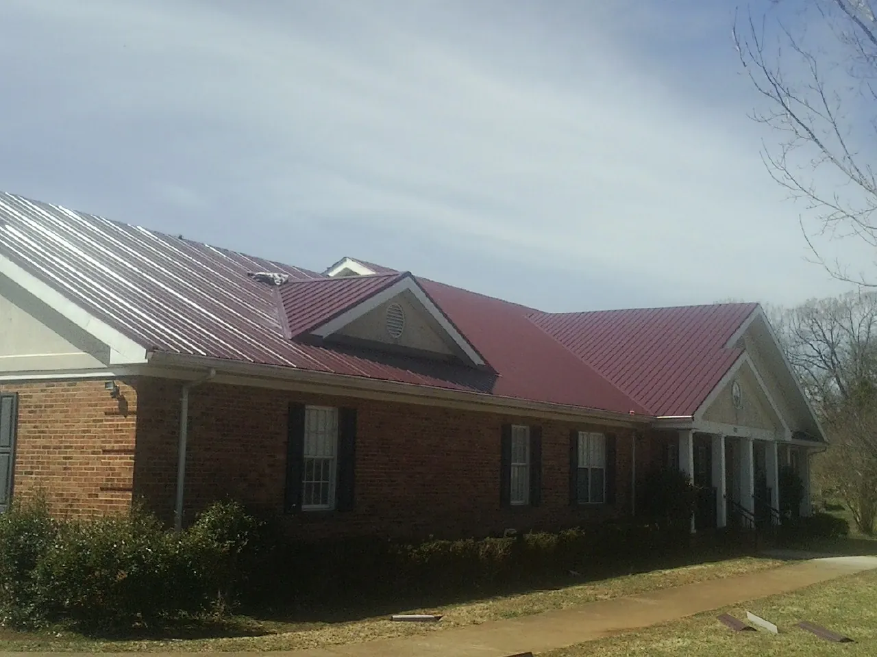 Red metal roof with gabled entries on a long brick building, from a Hail Damage Roof Repair job in South Plymouth