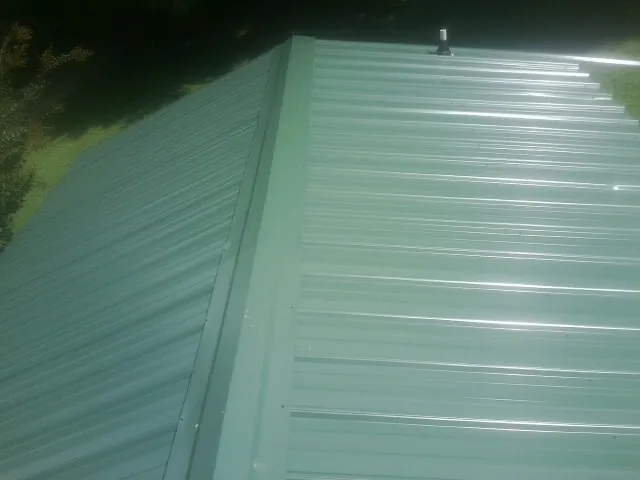 New green metal panels meeting at the ridge of a roof — Flat Roof Repair work by our crew in South Plymouth