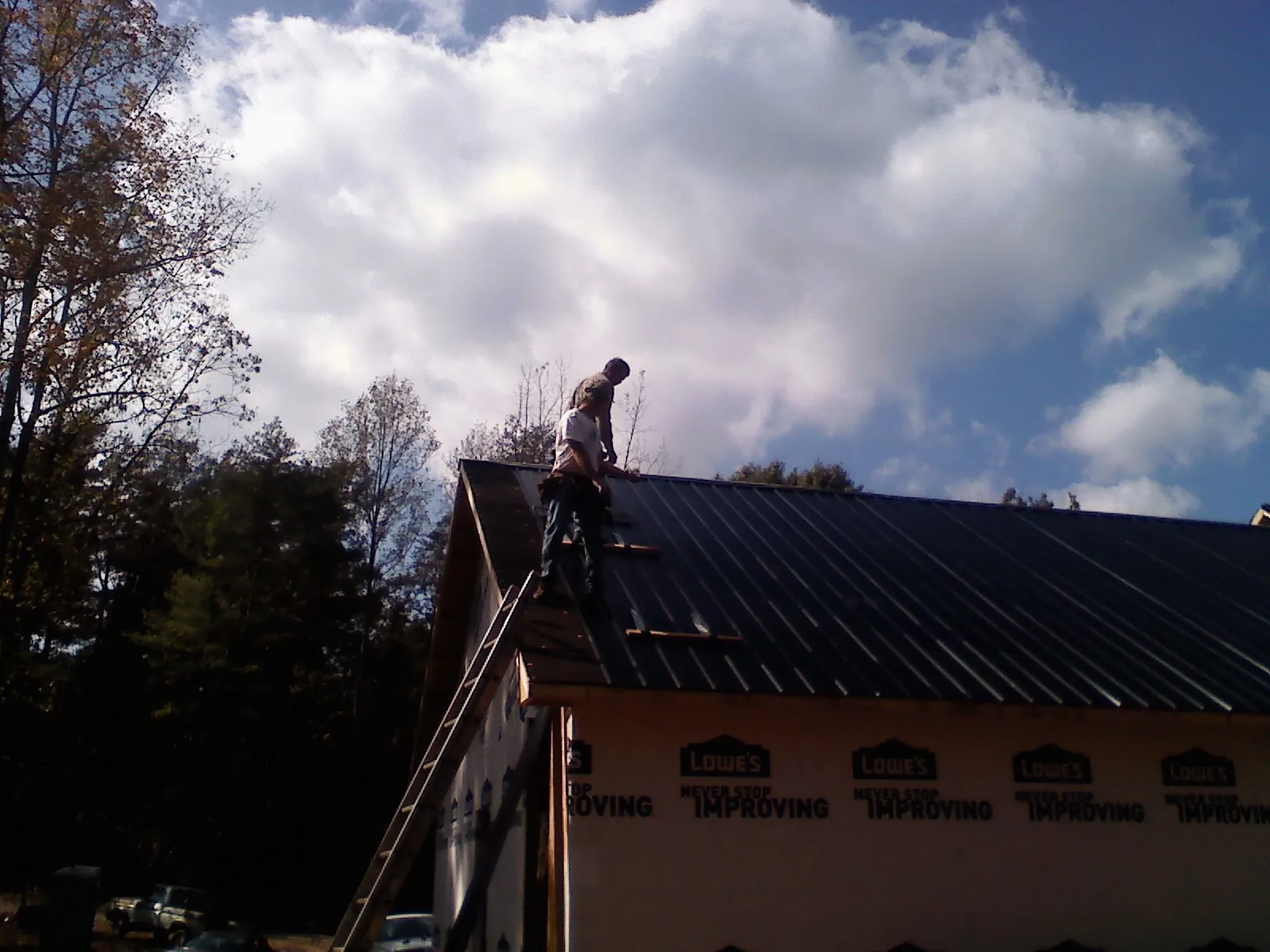 Roofer fastening dark metal panels high against a cloudy sky, from a Roof Inspection job in South Plymouth