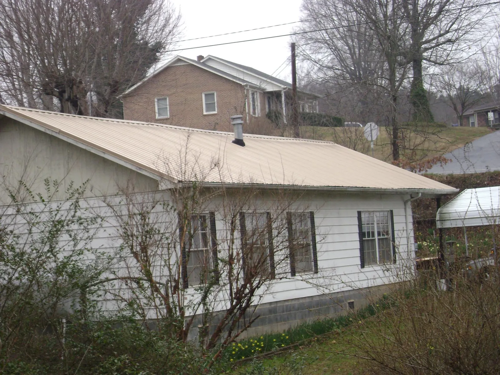 Tan metal roof on a white sided house set into a hillside — Commercial Roofing by Roofing Brothers in South Plymouth