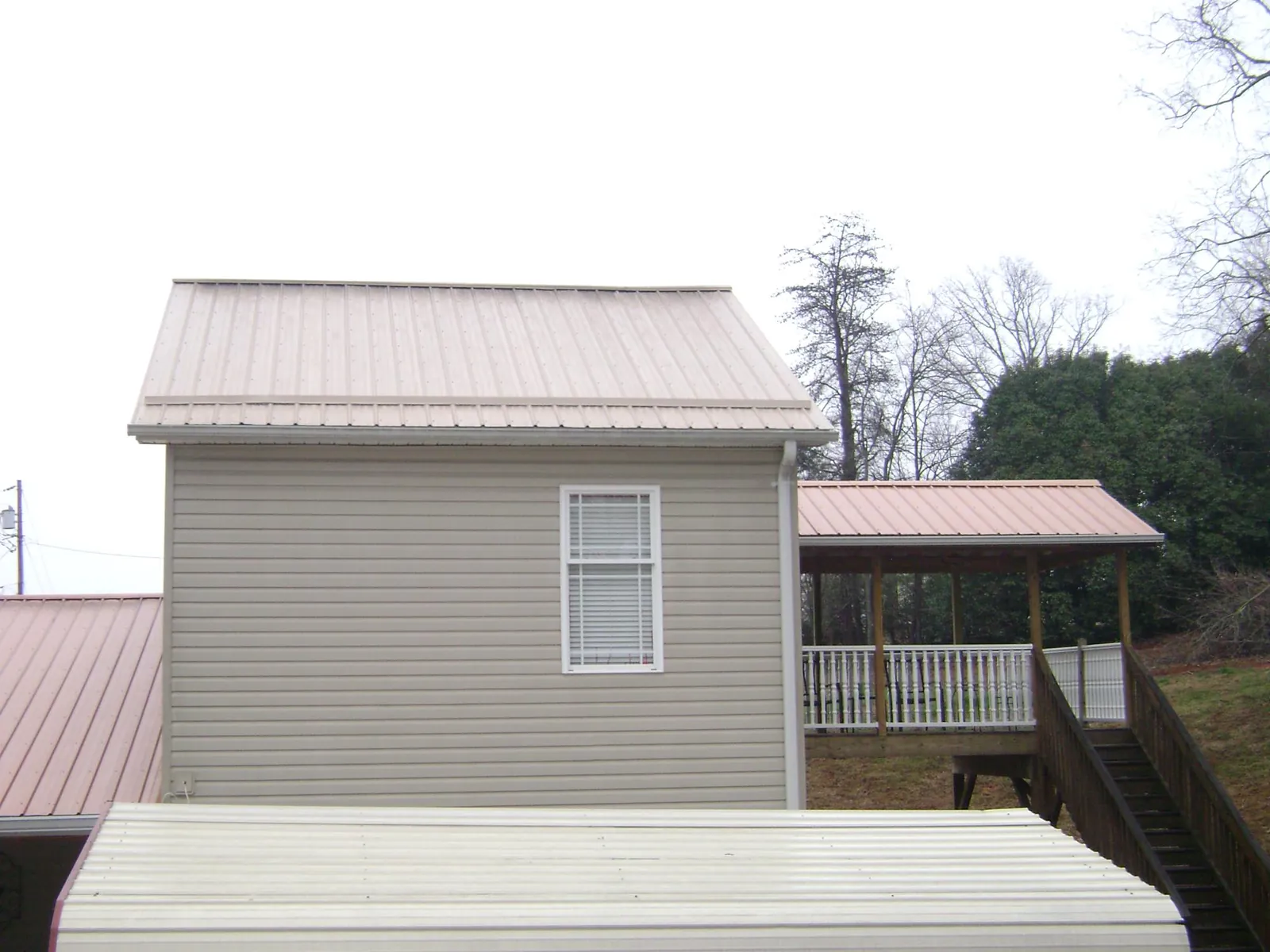 Tan metal roofs on a two story addition and attached porch, from a Roof Replacement job in South Plymouth